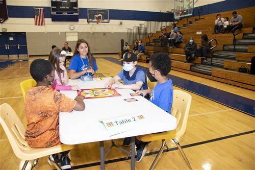 Four students seated at table in Annapolis high school gymnasium to compete in math 24 Game.